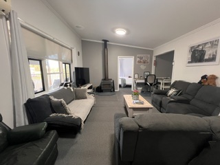 Open-plan lounge with wood heater, large corner lounges and TV in the 3 bedroom cottage - 3 Bedroom Cottage, Longhorn Ranch Apartments Orbost